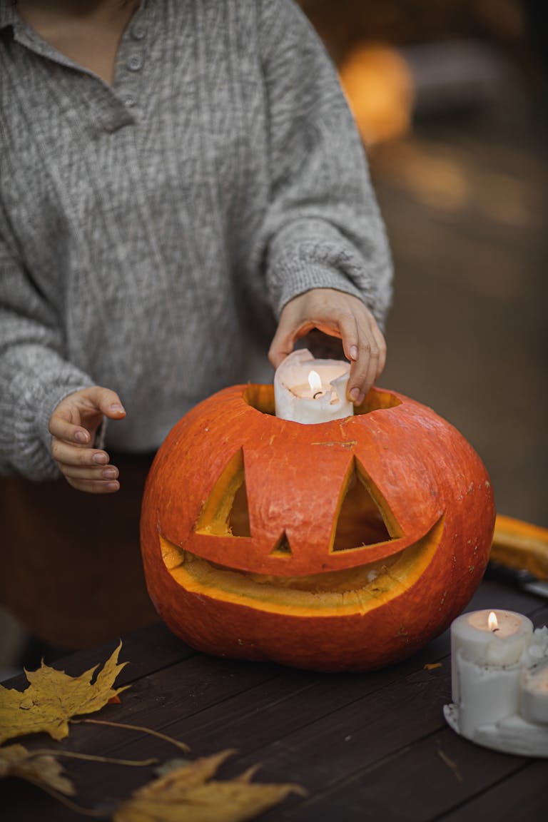 A woman places a candle inside a carved pumpkin outdoors for a festive Halloween decoration.