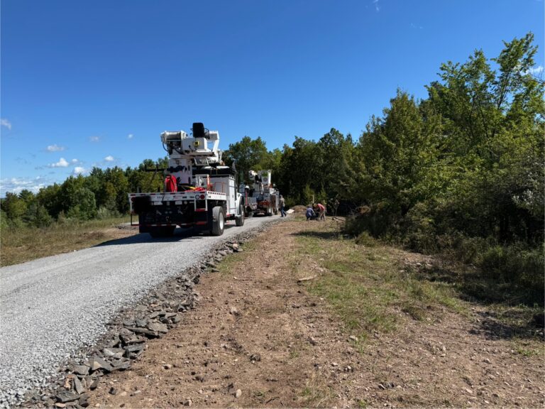 Power company trucks installing electricity lines on rural land, showing the process of bringing utilities to undeveloped property.